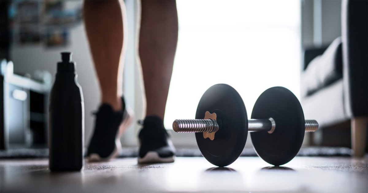 The lazy way to fitness - dumbbell, home workout and weight training concept. Man starting to exercise with dumbbell. Water or protein shake bottle on floor.