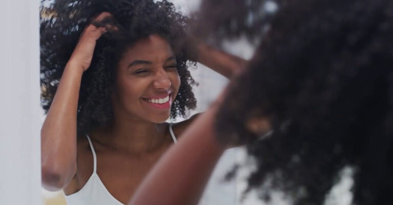 Woman smiling in the mirror after using Kintone batana oil to nourish her afro curls